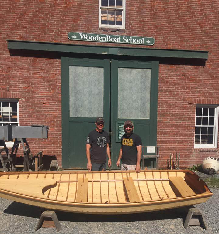 two men standing in front of a wooden pram built at wooden boat school